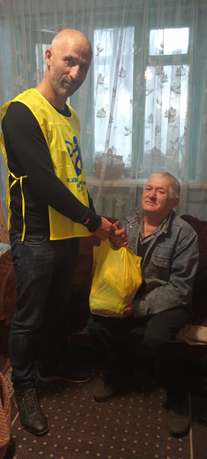 A team member shaking hands with a seated man who holds a yellow bag of supplies.